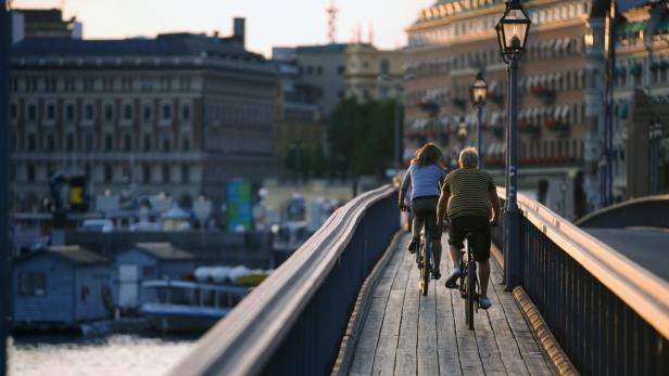 Zwei Personen fahren mit Fahrrädern über eine Brücke in einer Stadt.