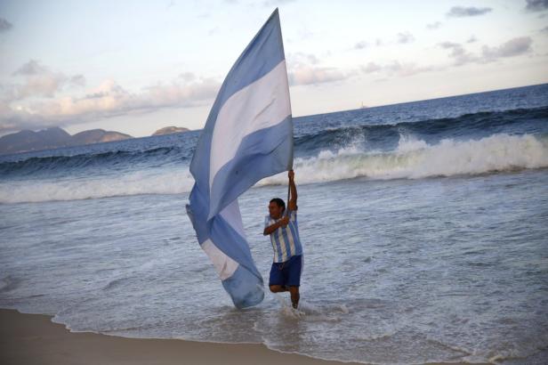 Ein Mann steht am Strand im Wasser und hält eine große argentinische Flagge hoch.