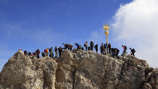 Viele Wanderer auf dem Gipfel der Zugspitze mit goldenem Gipfelkreuz.