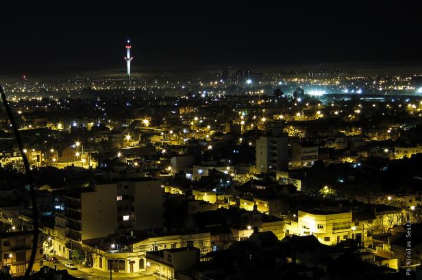 Nachtsicht auf eine Stadt mit einem beleuchteten Turm im Hintergrund.