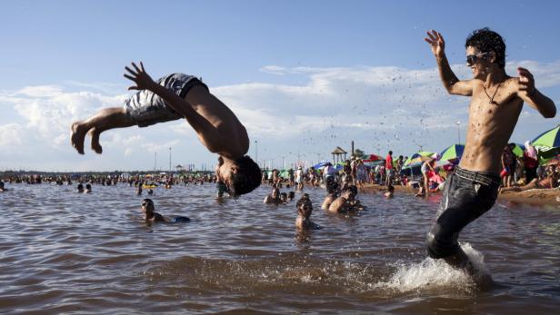 Ein Mann macht einen Salto ins Wasser, während ein anderer am Ufer jubelt.