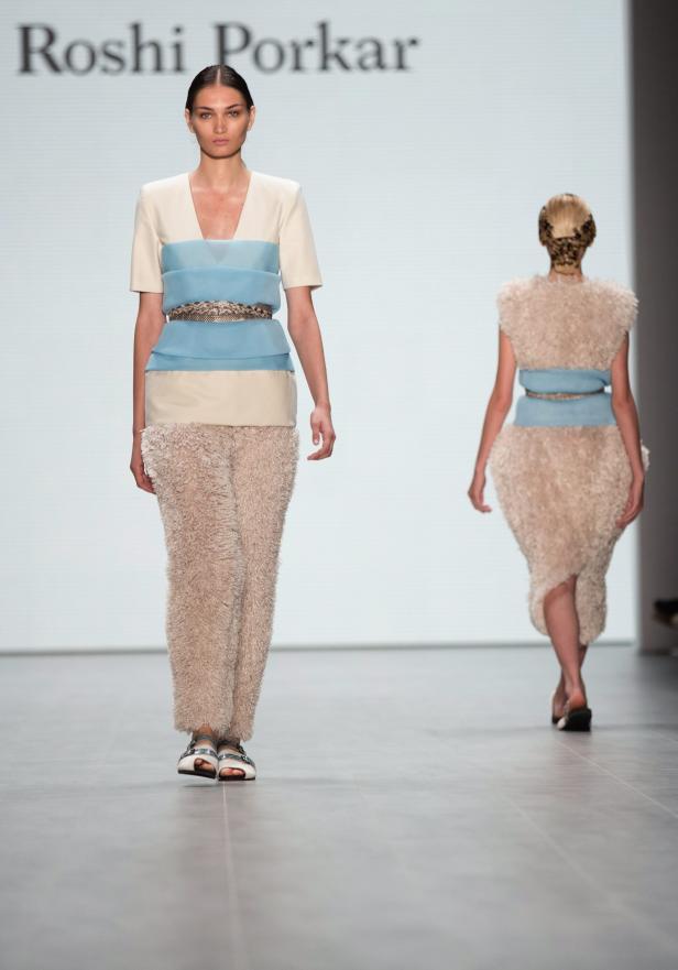 Eine Frau präsentiert ein beiges Outfit mit blauen Akzenten auf dem Laufsteg.