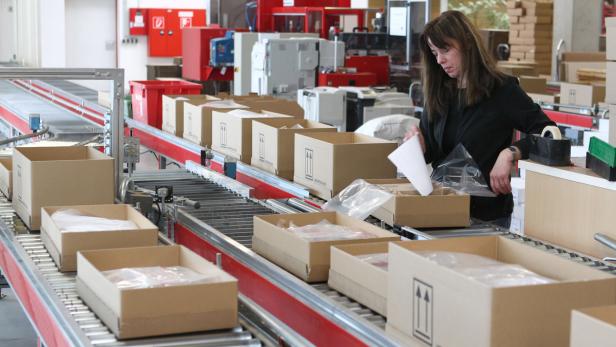 Eine Frau verpackt Waren in Kartons an einem Förderband.