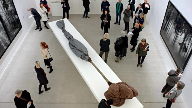 Besucher betrachten eine Skulptur und Fotografien in einer Kunstgalerie.