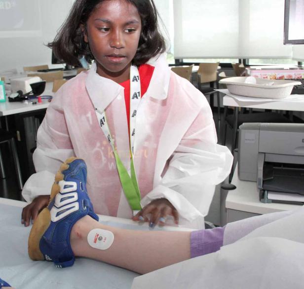 Ein Mädchen im Laborkittel untersucht ein Bein mit einem Sensor.