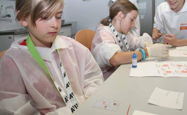 Kinder in Laborkitteln führen einen Blutgruppentest durch.