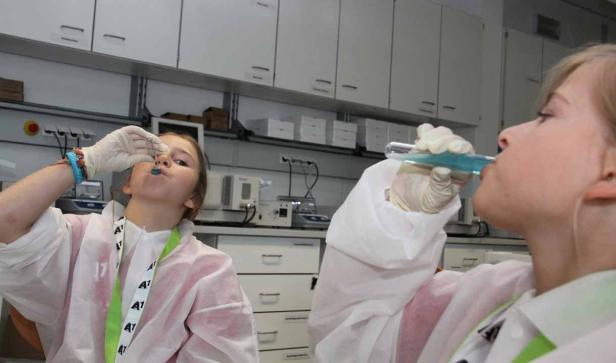 Zwei Personen in Laborkitteln scheinen blaue Flüssigkeiten zu probieren.