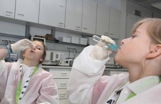 Zwei Mädchen im Labor trinken blaue Flüssigkeit aus Reagenzgläsern.