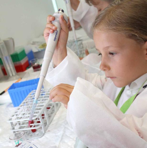 Ein Mädchen im Laborkittel pipettiert eine Flüssigkeit in ein Reagenzglas.