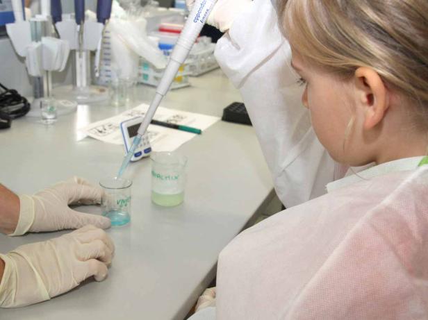 Ein Mädchen im Laborkittel pipettiert eine Flüssigkeit in ein Becherglas.