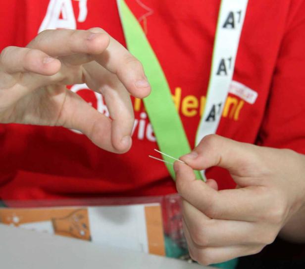 Eine Person hält zwei dünne, weiße Drähte in den Händen.