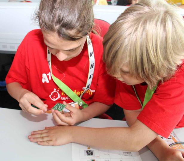 Zwei Kinder in roten T-Shirts arbeiten an einer elektronischen Schaltung.