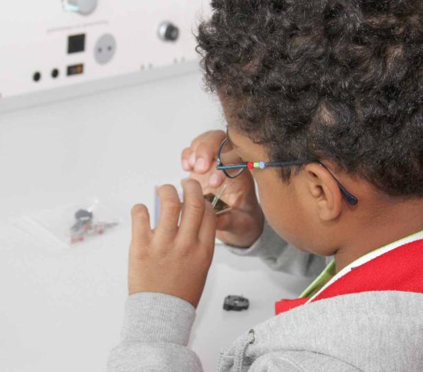 Ein Kind mit Brille untersucht elektronische Bauteile auf einem Tisch.