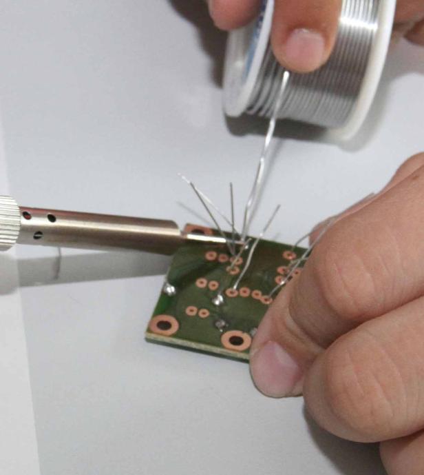 Eine Person lötet mit Lötzinn eine kleine Platine.