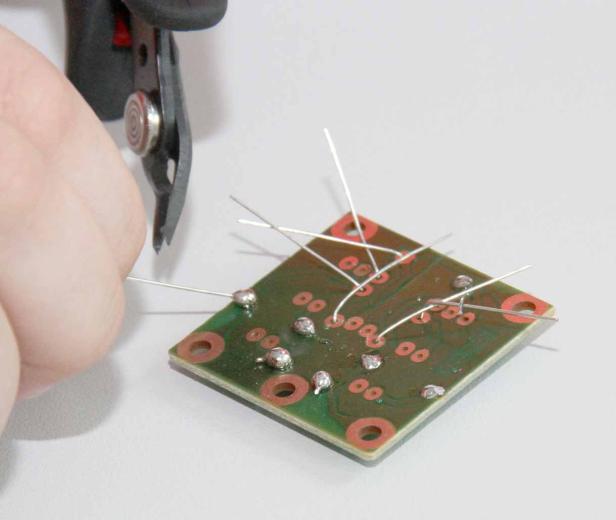 Eine Person schneidet die Drähte einer bestückten Platine ab.