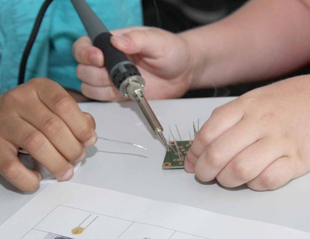 Eine Person lötet Bauteile auf eine grüne Platine.
