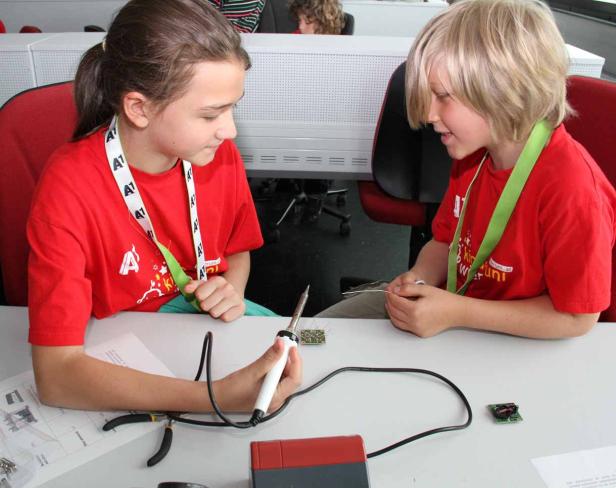 Zwei Kinder löten gemeinsam an elektronischen Bauteilen.