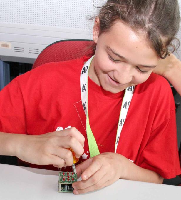 Ein Mädchen schraubt an einer kleinen elektronischen Platine.