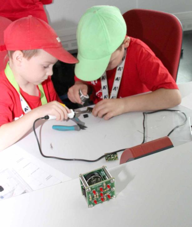 Zwei Kinder löten an einem elektronischen Bauteil.