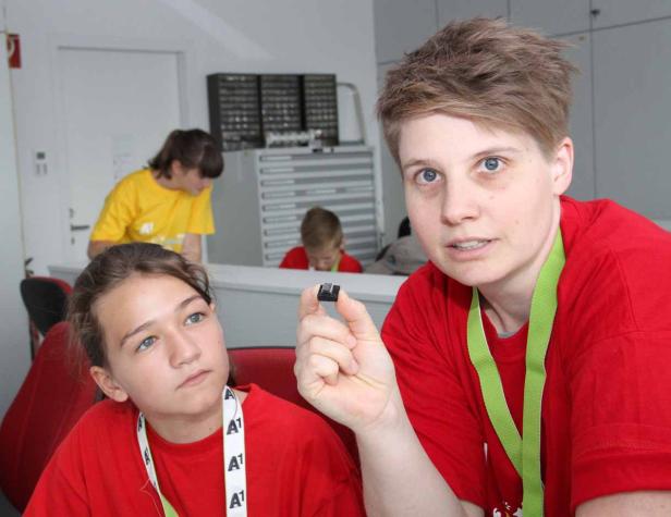 Eine Frau zeigt einem Mädchen einen kleinen Chip, während andere Kinder im Hintergrund zu sehen sind.
