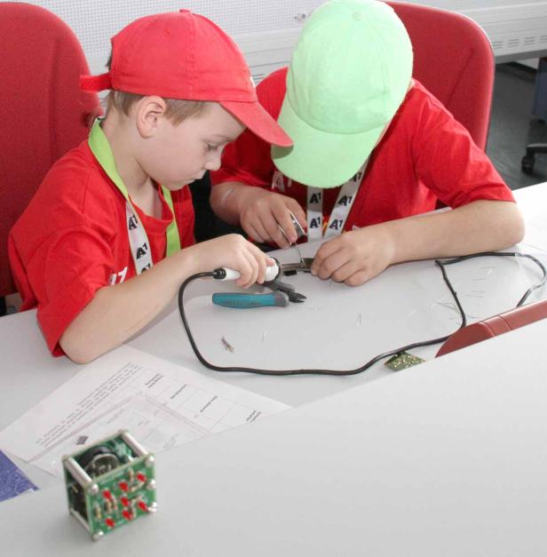 Zwei Kinder löten an einem Tisch mit Werkzeug und Schaltplänen.