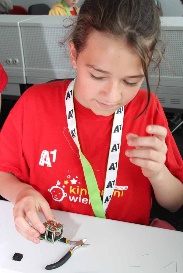 Ein Mädchen bastelt mit einer kleinen elektronischen Schaltung und einer Zange.