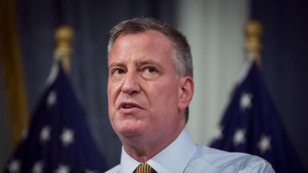 Bill de Blasio spricht vor zwei unscharfen Flaggen.