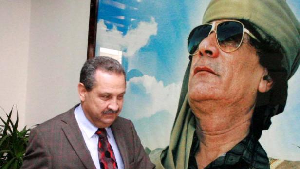 Ghanem war von 2003 bis 2006 libyscher Ölminister. Ein Mann in einem Anzug steht neben einem Porträt von Muammar al-Gaddafi.