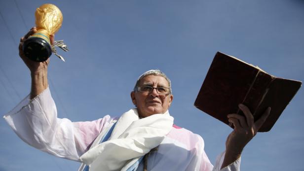Ein Mann im Papstkostüm hält eine Weltmeisterschaftstrophäe und ein Buch in die Höhe.