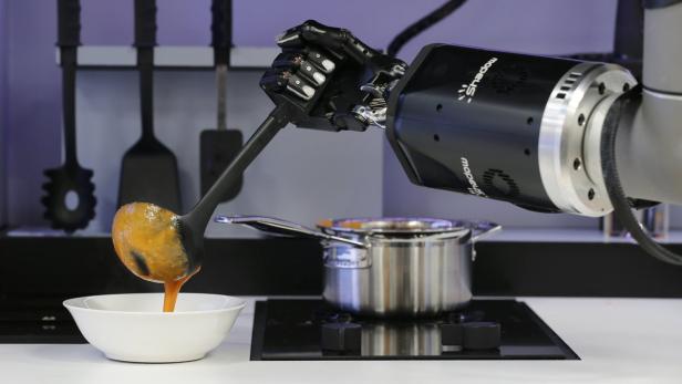 Ein Roboterarm gießt mit einer Schöpfkelle Suppe in eine Schüssel.