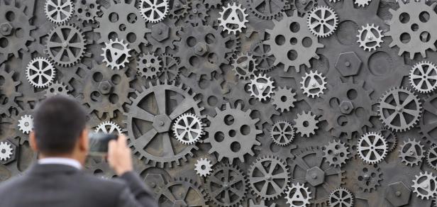 Ein Mann fotografiert eine Wand voller Zahnräder.