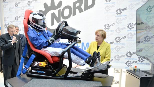 Angela Merkel beobachtet eine Person in einem Rennsimulator.