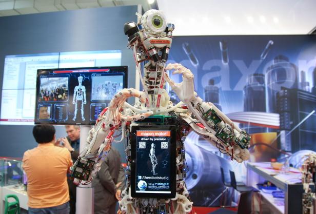 Ein humanoider Roboter mit freiliegender Mechanik steht auf einer Messe.