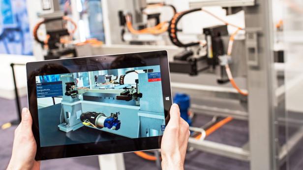 Eine Person hält ein Tablet, das eine 3D-Simulation einer Produktionsanlage zeigt.