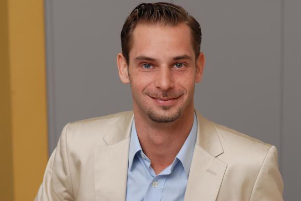 Ein Mann mit hellblauen Augen und Sakko lächelt in die Kamera.