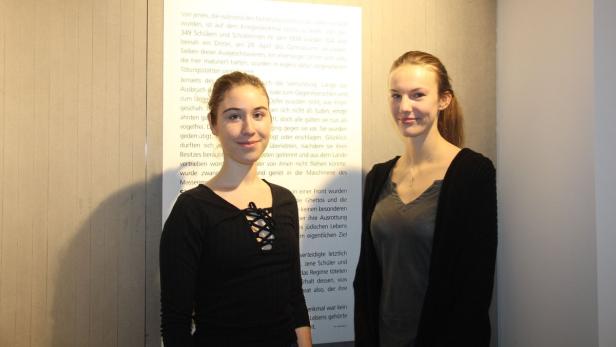 Zwei junge Frauen stehen vor einer Wand mit einem Text über die NS-Zeit.