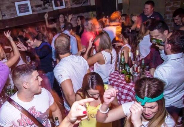 Menschen tanzen und feiern in einer Bar mit Tischen voller Getränke.
