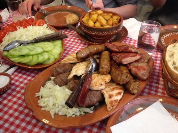 Eine Platte mit gegrilltem Fleisch, Würstchen und Gemüse auf einem rot-weiß karierten Tisch.