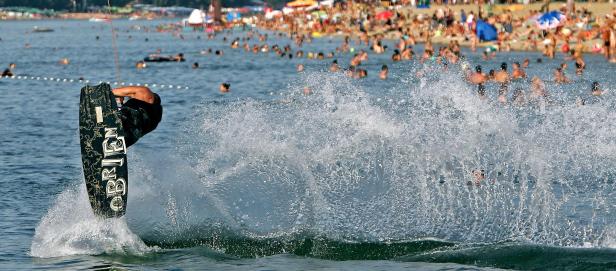 Ein Wakeboarder springt über das Wasser vor einem belebten Strand.