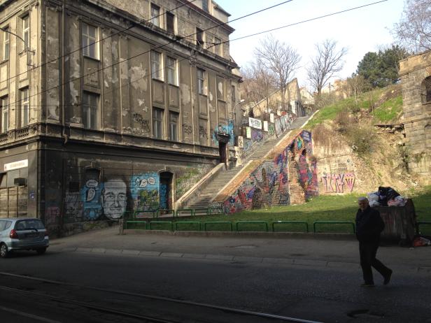 Ein Mann geht eine Straße entlang, im Hintergrund eine Treppe mit Graffiti an einem alten Gebäude.