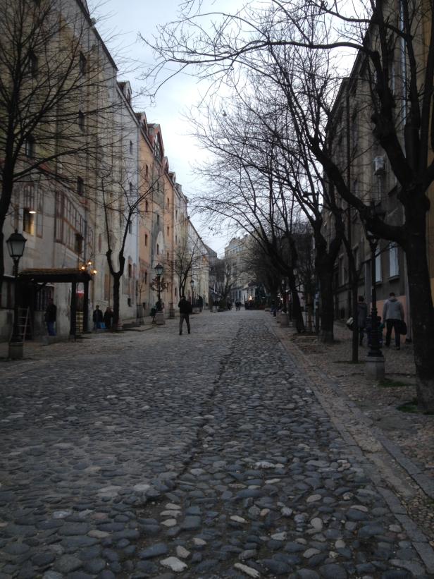 Eine Kopfsteinpflasterstraße in einer europäischen Stadt mit Menschen und alten Gebäuden.