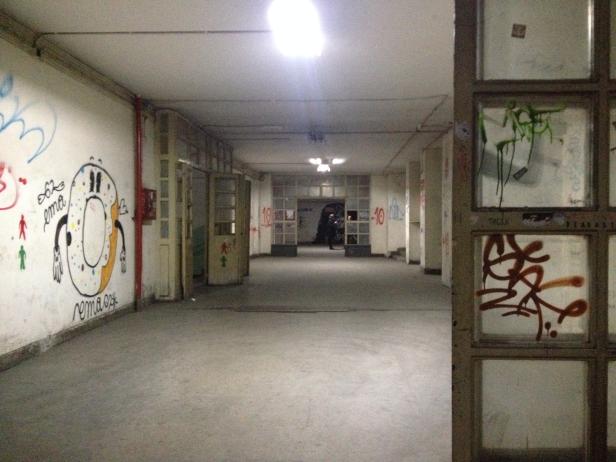 Ein langer, leerer Flur mit Graffiti an den Wänden und Türen.