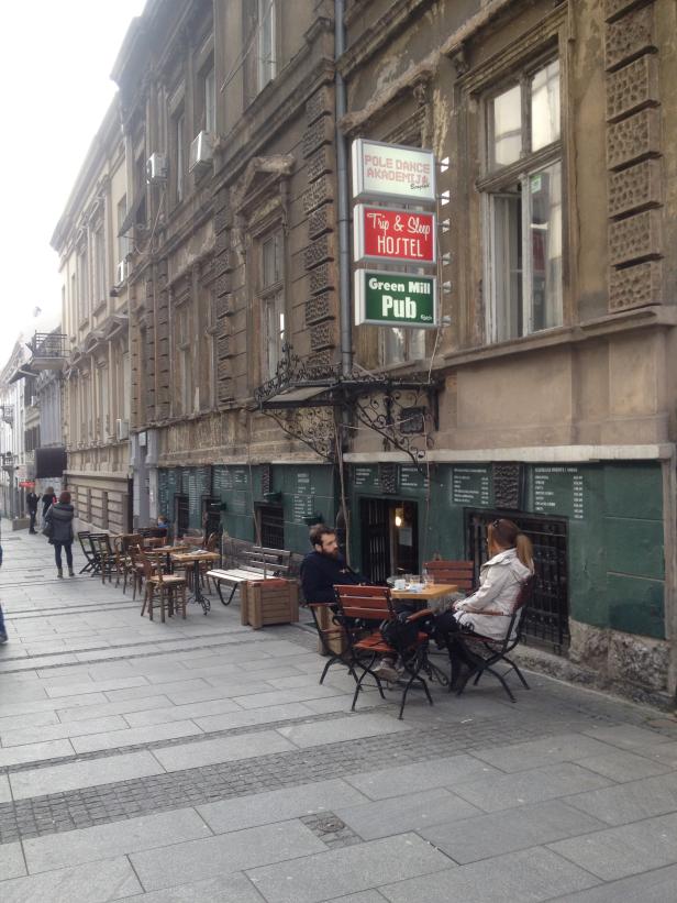 Ein Paar sitzt vor dem „Green Mill Pub“ und dem „Trip & Sleep Hostel“ in Belgrad.