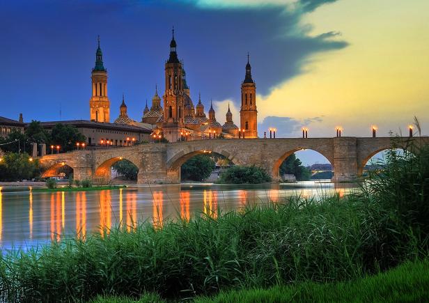 Die Basílica del Pilar und eine Steinbrücke über den Ebro in Saragossa bei Dämmerung.