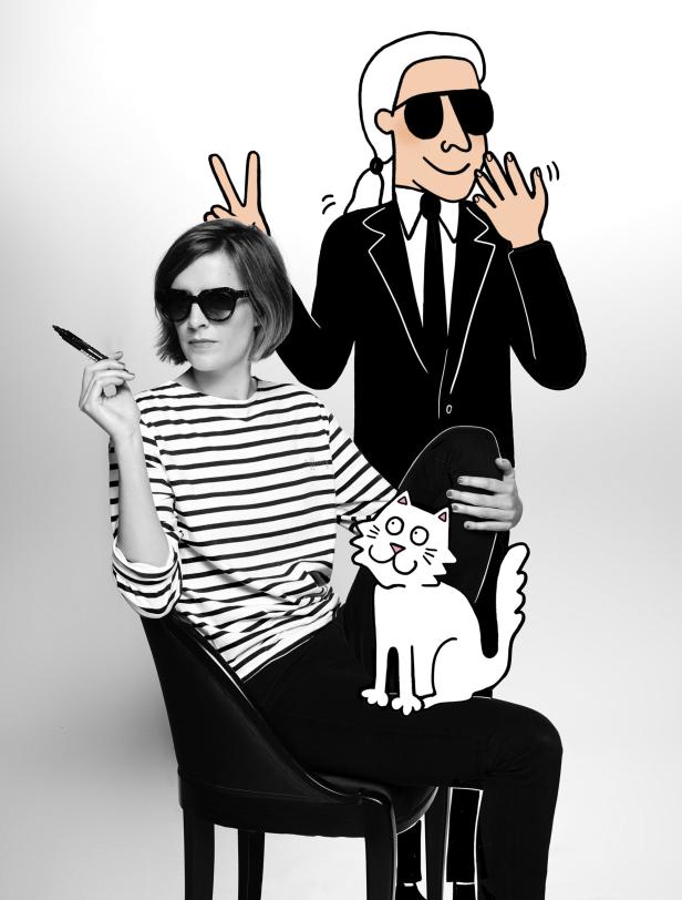 Eine Frau mit Sonnenbrille sitzt mit einer Cartoon-Version von Karl Lagerfeld und einer Katze im Schoß.