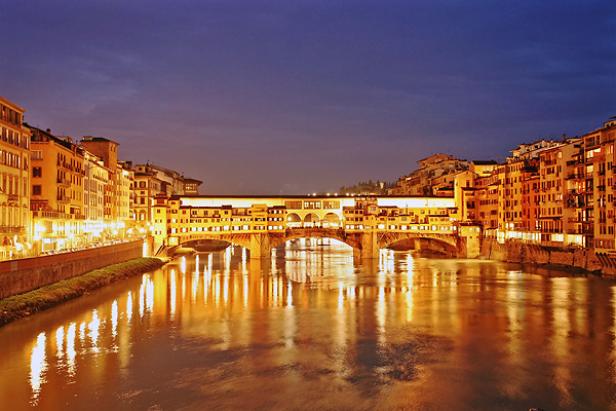 Die Ponte Vecchio in Florenz spiegelt sich nachts im Arno.