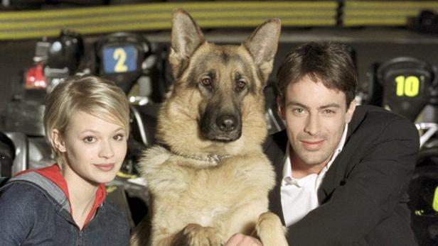 Eine junge Frau, ein Schäferhund und ein Mann posieren vor Go-Karts.
