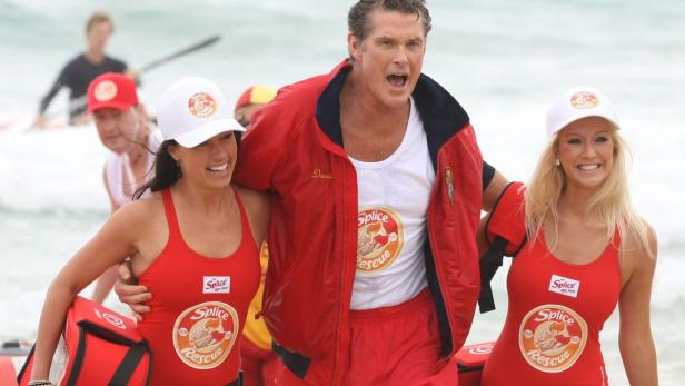 David Hasselhoff umarmt zwei Rettungsschwimmerinnen am Strand.