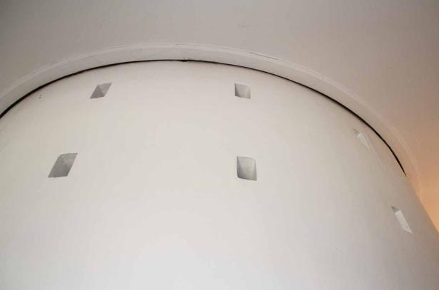Eine weiße, gewölbte Wand mit quadratischen Öffnungen unterhalb einer Decke.