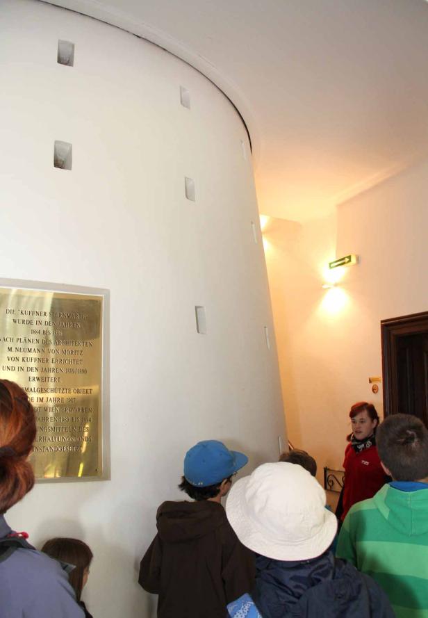 Eine Gruppe von Personen steht in einem Gebäude vor einer Gedenktafel der Kuffner-Sternwarte.